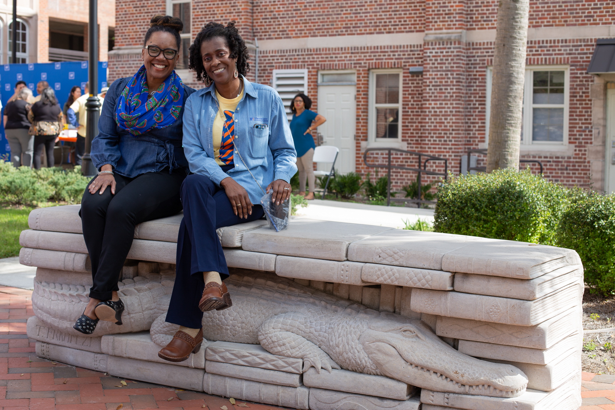 Two people sitting on a bench with a gator engraving on it and smiling at the camera