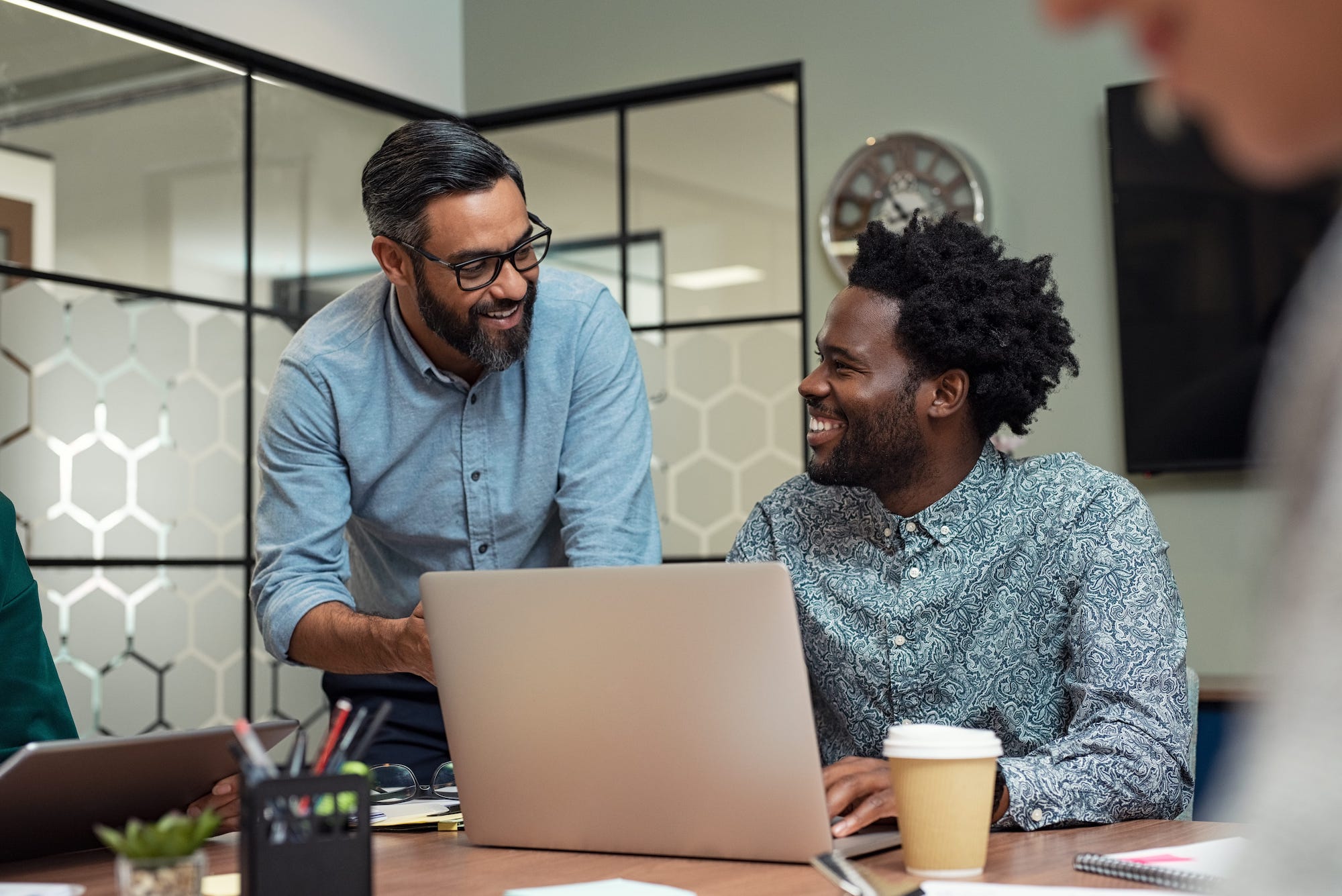 AdobeStock_233745515 2 people taking to each other in a conference room. one of them is using a laptop.